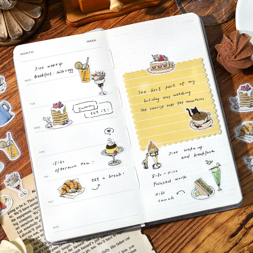 Open planner with illustrated food and drink pages on a wooden surface