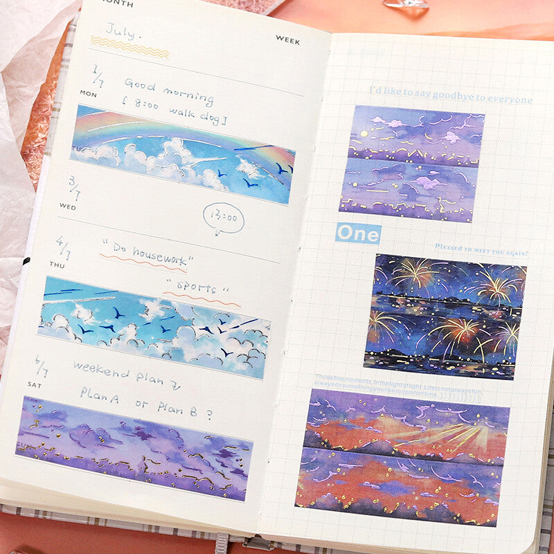 Open planner with illustrated pages of a blue sky, clouds, and fireworks.