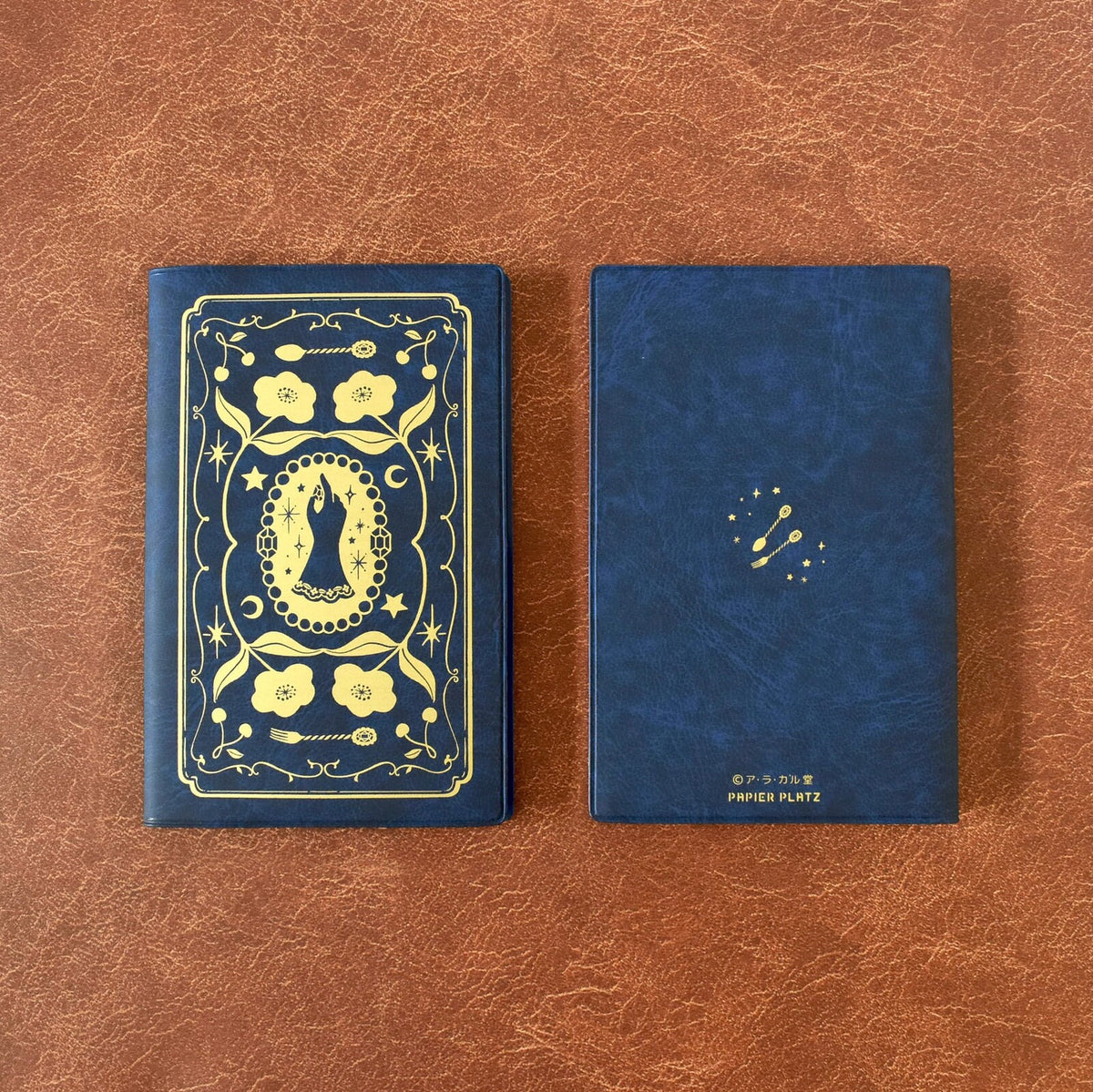 2 Blue plastic covered notebook with gold foil design on a leather background