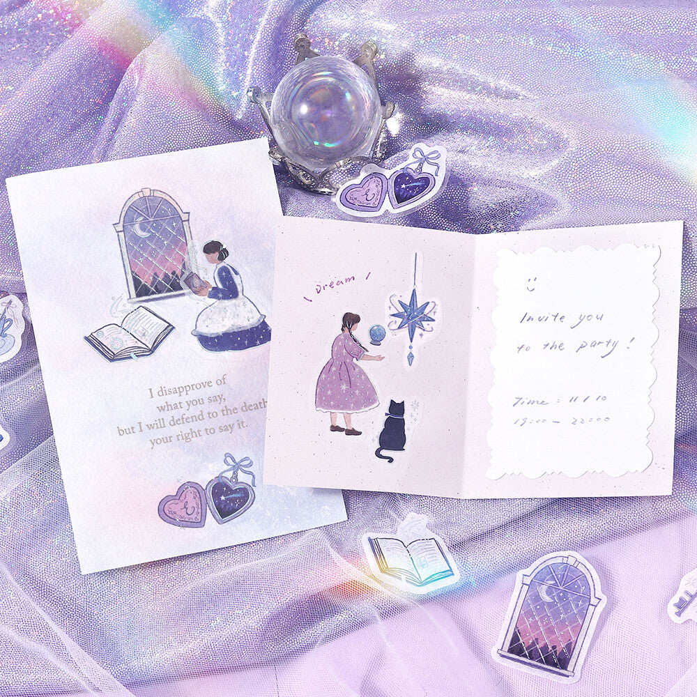 A styled flat-lay of two illustrated invitation cards on iridescent lavender fabric, surrounded by matching heart-shaped and window-shaped stickers and a crystal ball.