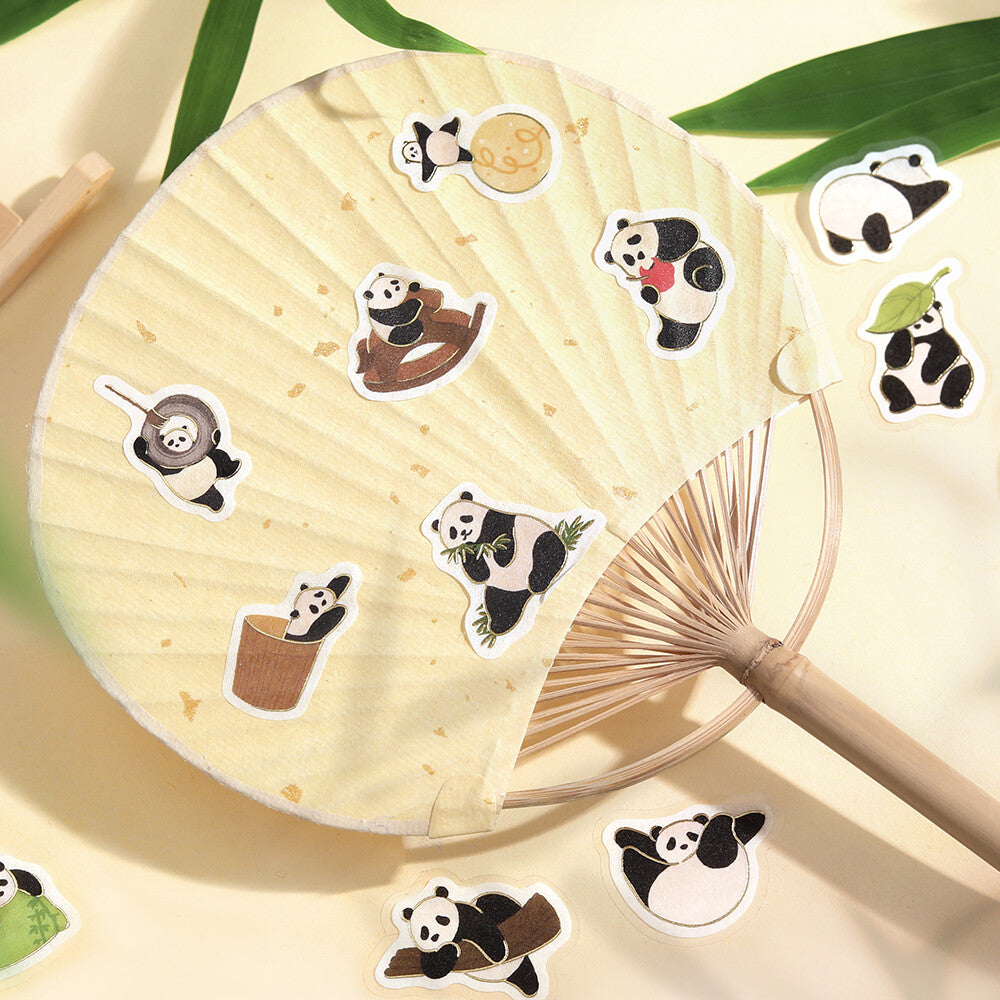 Set of panda-themed stickers on a wooden fan with green leaves in the background