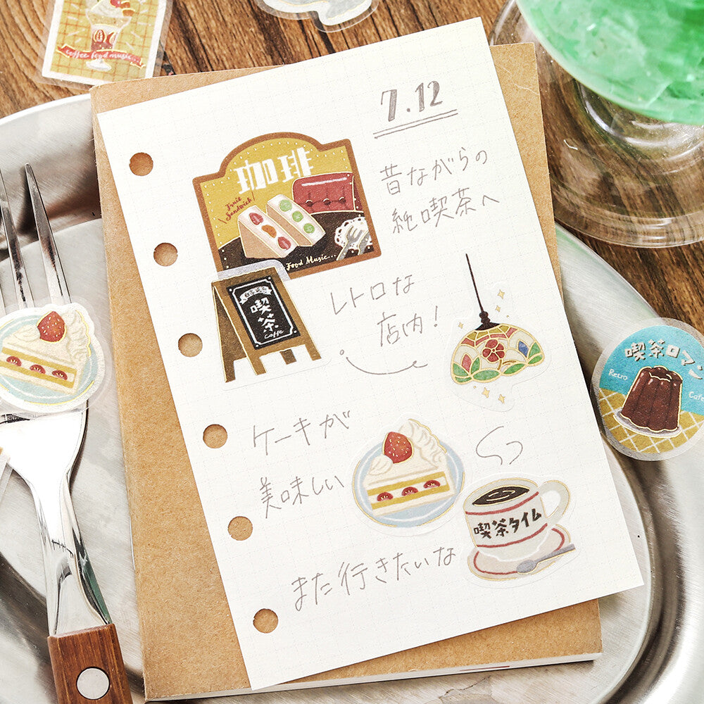 Card with illustrations of a bakery and Japanese text on a wooden table with a drink and cake.