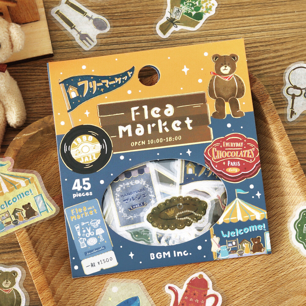 A package of BGM Inc. Flea Market themed sticker sheets displayed on a wooden surface surrounded by other loose stickers.