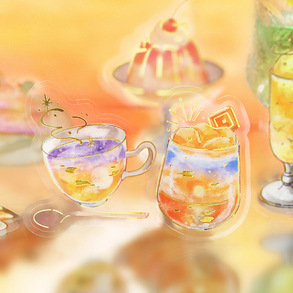 A soft, warm-toned illustration showing two translucent dessert-themed drink glasses with layered pastel colors and small gold leaf accents, alongside a spoon and blurred desserts in the background.