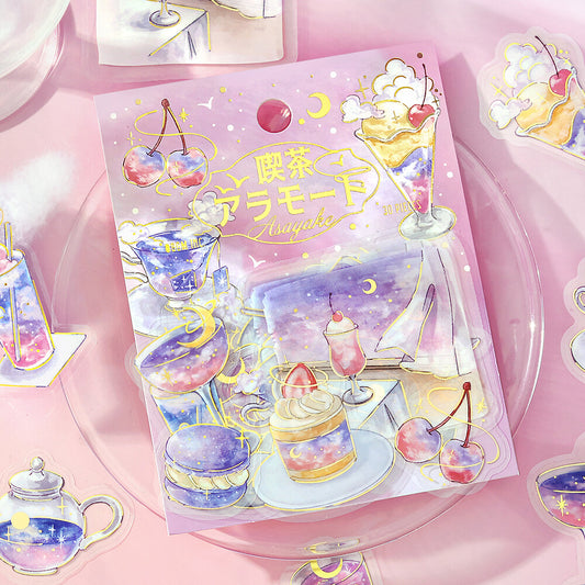 A pastel pink illustrated sticker sheet or sticker pack featuring desserts, teacups, cherries, and celestial motifs, displayed on a clear round plate with matching stickers around it.