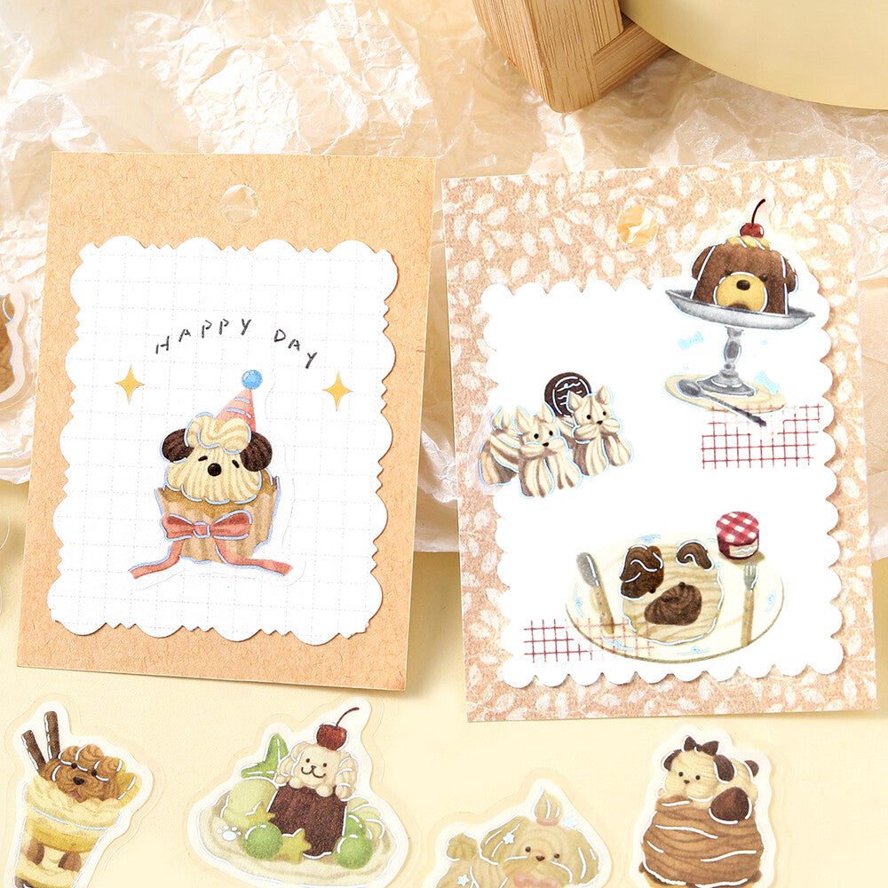 A set of cute cartoon dog dessert-themed stickers or decals arranged on a light beige surface, including a cupcake, donut, ice cream sundae, and chocolate cake designs on scalloped white labels over patterned backing cards.