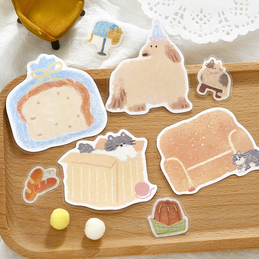 A set of cute, die-cut paper stickers featuring cozy home and pet illustrations, arranged on a light wooden tray with small decorative props.