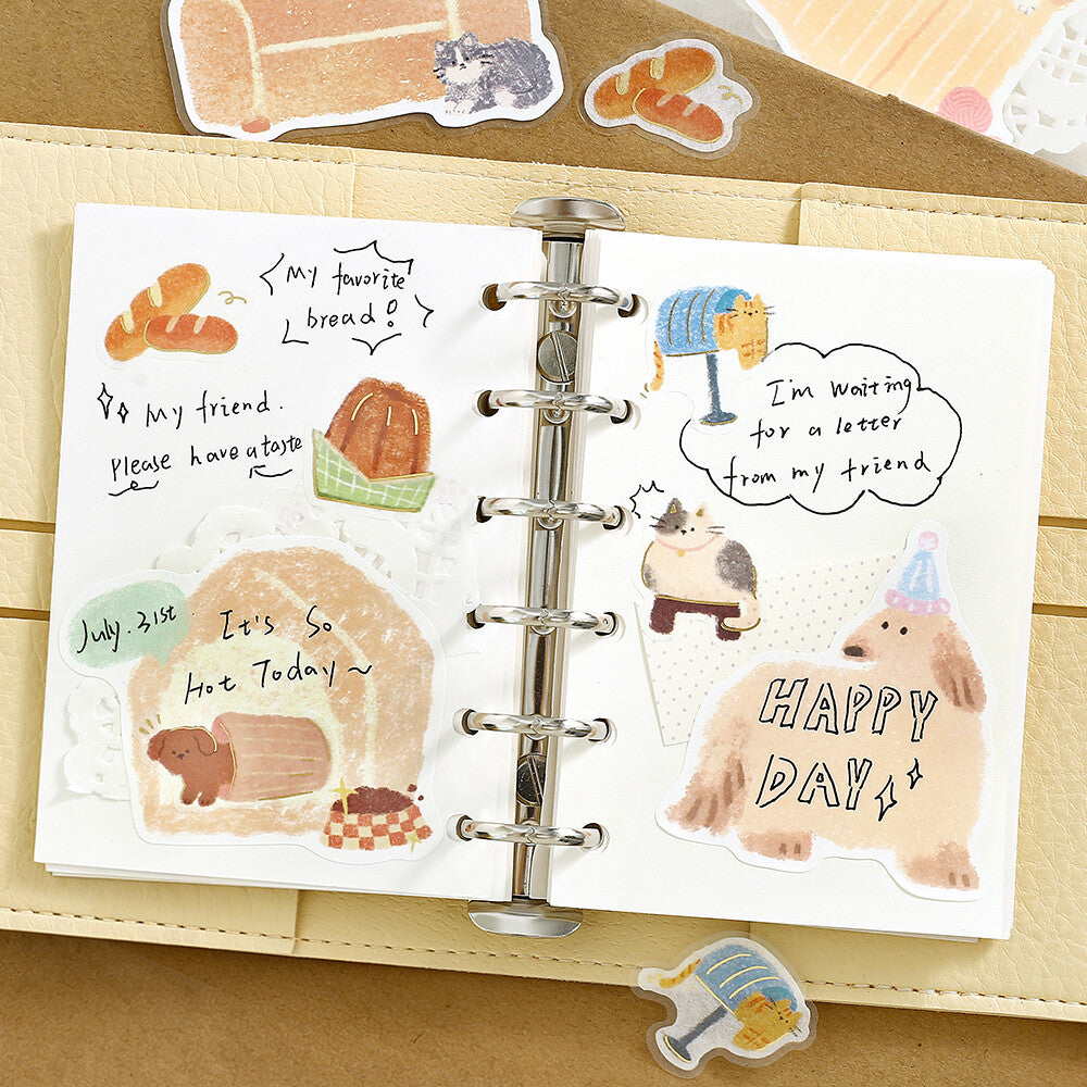 Planner with stickers featuring bread, animals, and text on a wooden surface