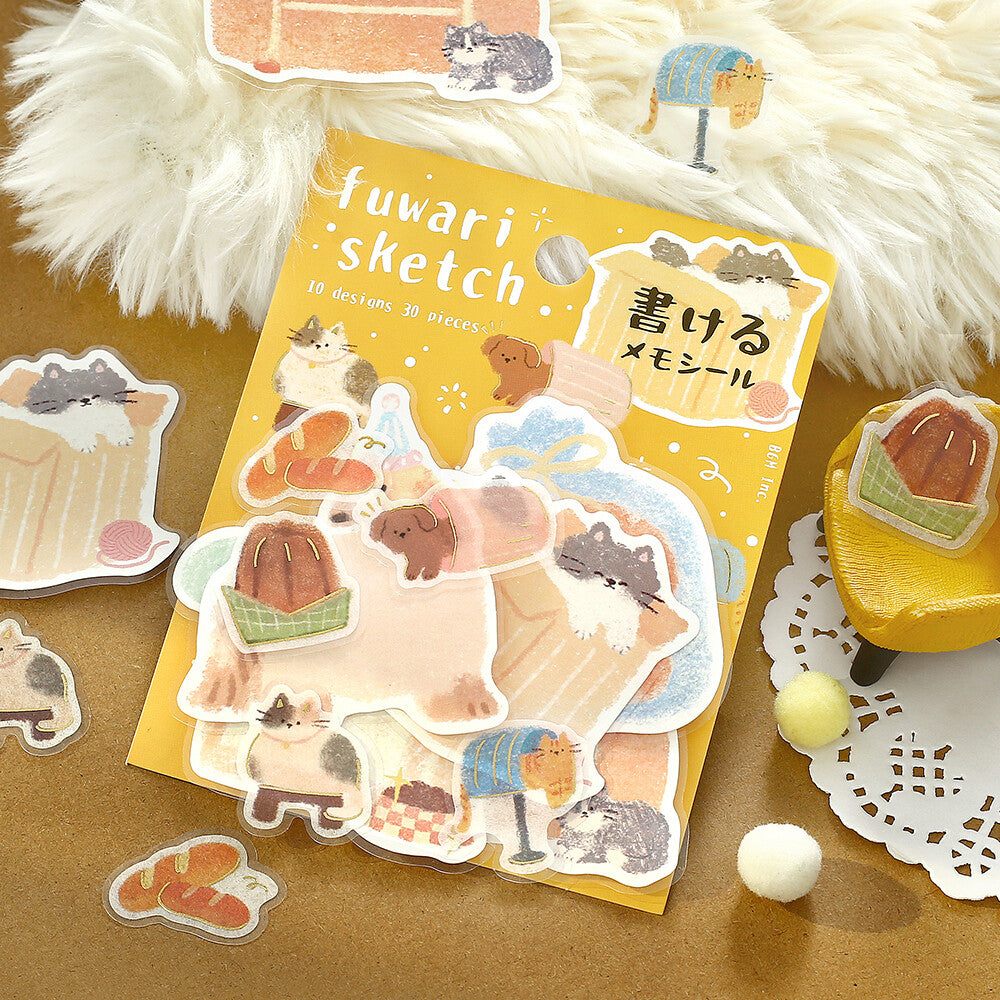 A package of cute animal-themed stickers labeled 'fuwari sketch' is arranged on a brown surface with several individual stickers placed around it. The stickers feature pastel illustrations of cats, dogs, and small animals in cozy settings, with a yellow package and soft decorative props including faux fur, a small chair, and pom-poms.