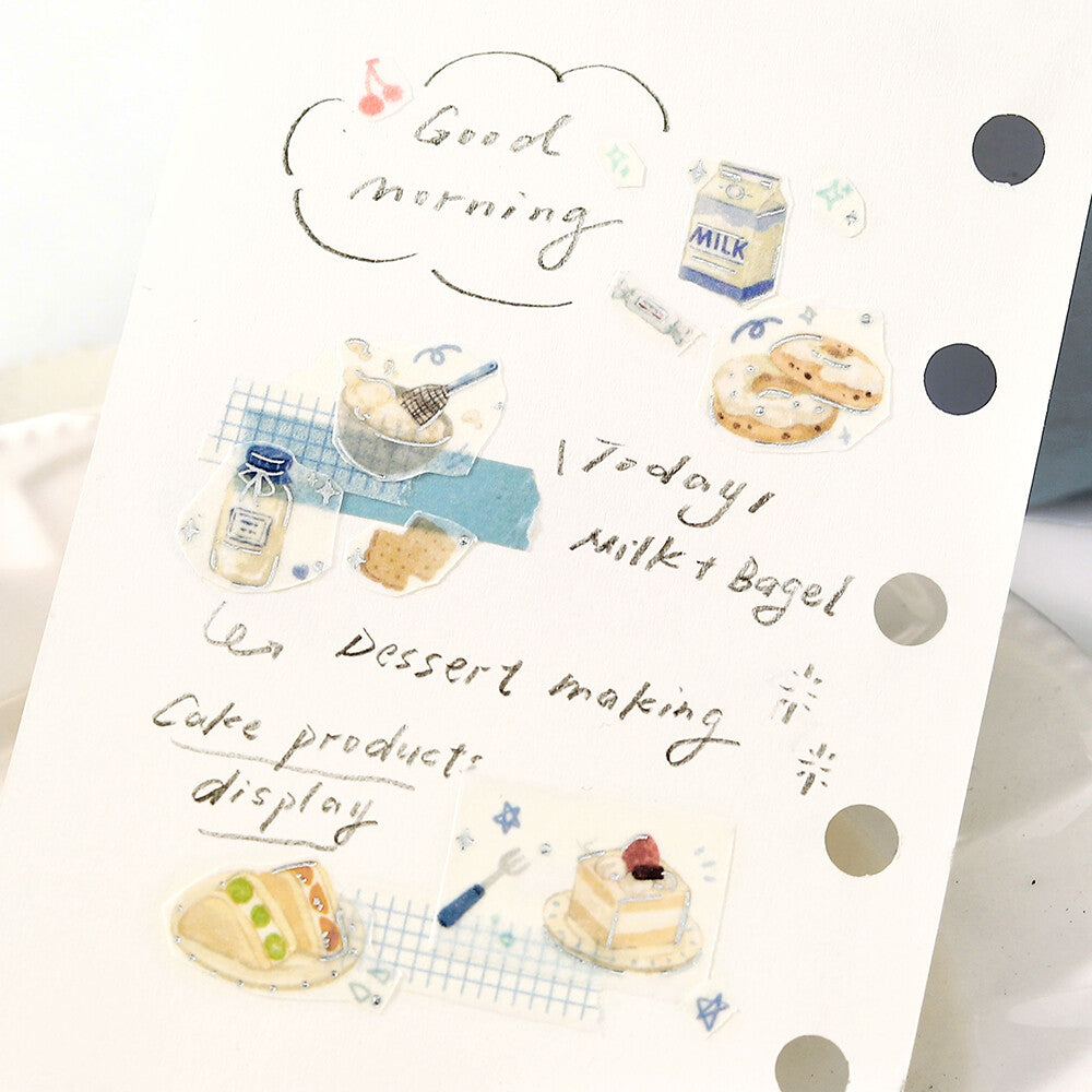 Notebook page with illustrations of milk, bagels, and cakes, and text about a morning routine.