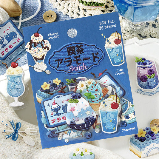 A sheet of brunch-themed cake and dessert stickers from BGM Inc. is displayed on a white tray alongside a matching red-and-white checkered napkin, a glass of iced coffee, and other cake illustrations.