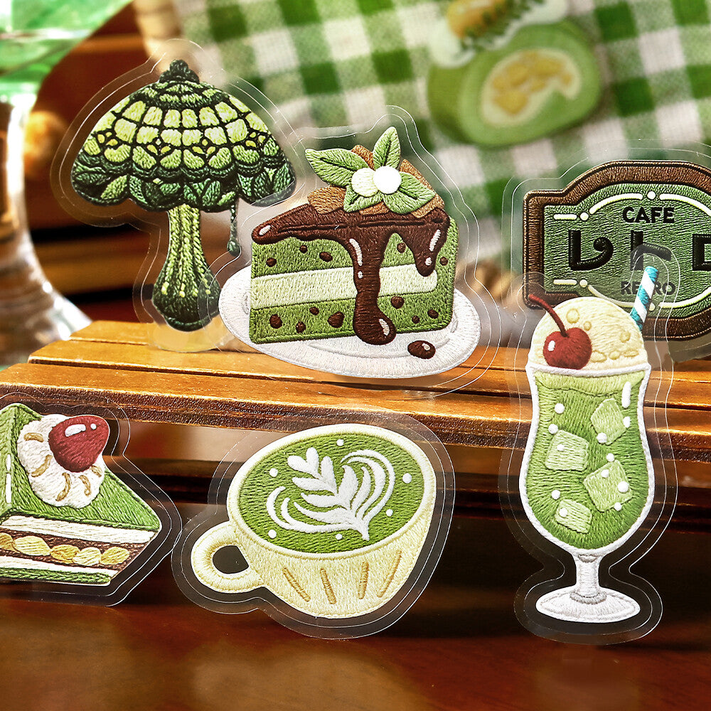 Cafe themed stickers displayed in a row on a textured wood desk background. The stickers feature various retro-themed desserts, drinks, and signage in shades of green, cream, and red.