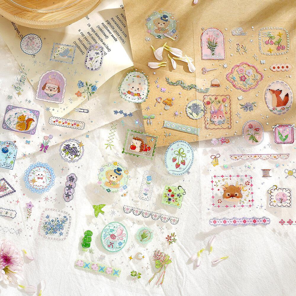 Three decorative sticker sheets labeled with pastel cartoon illustrations and small decorative elements, shown on a pile of papers in the background