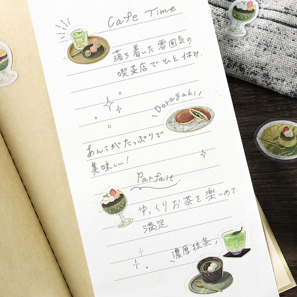 Sheet of paper with Japanese text and illustrations of tea and sweets on a wooden surface.