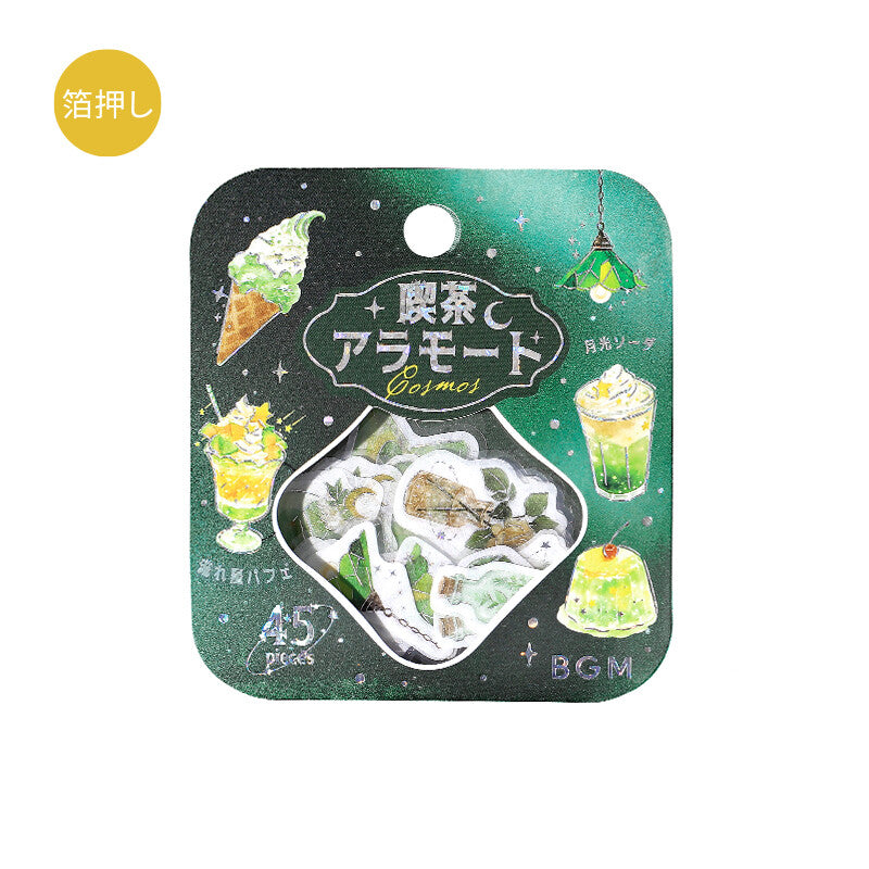 A packaged cosmetic sticker set on a white background. The product is in a rounded square black card with a green space-themed design, featuring illustrations of green drinks and desserts, and a central clear window showing the white and green cosmetic stickers inside.