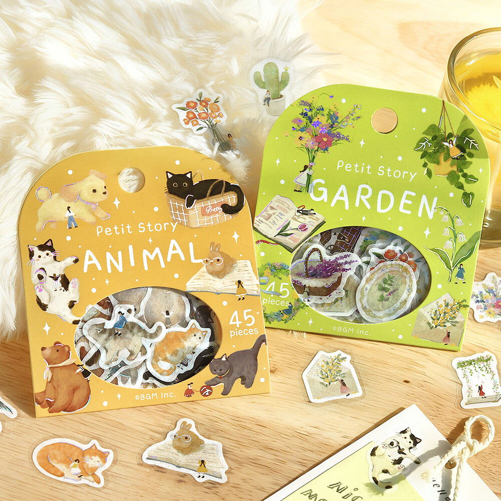 Two packages of Petit Story stickers, one with animal designs and the other with garden-themed designs, on a wooden surface.