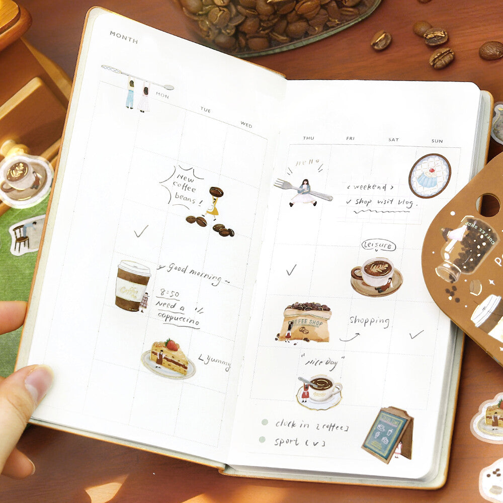 Notebook with illustrated coffee-themed stickers on a wooden surface with coffee beans.