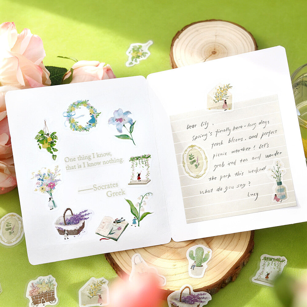 Open book with decorative stickers on a green surface with flowers and wood slices.