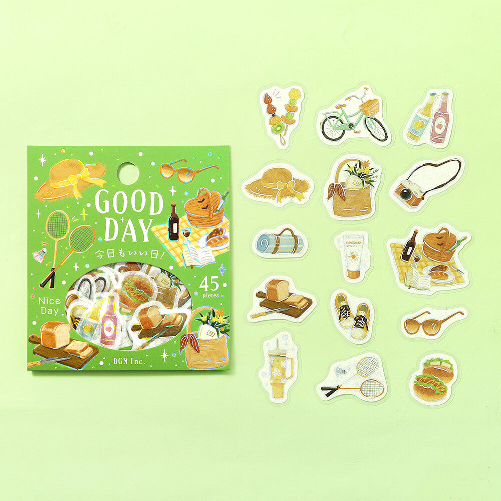A set of good day themed stickers displayed next to their packaging on a flat green background. 