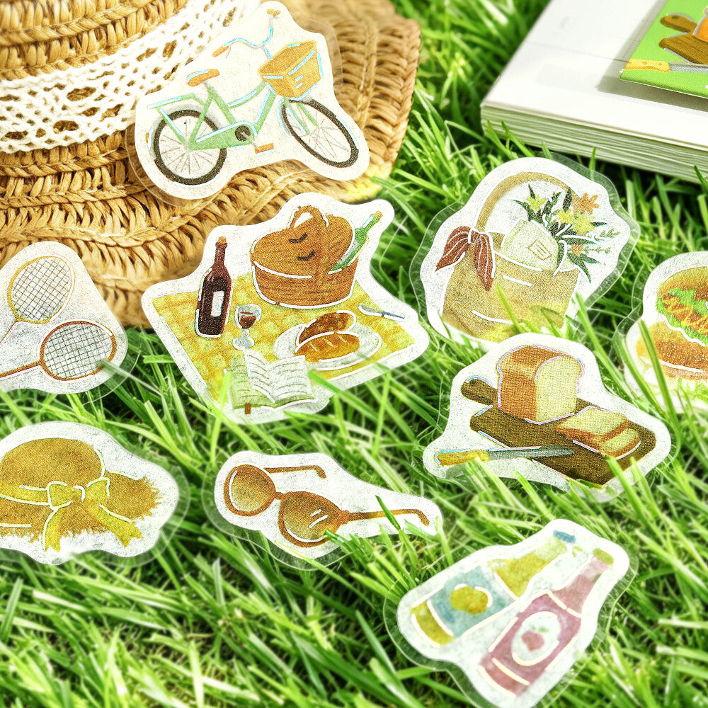 A close-up of a sliced bread or pastry topped with cute illustrated stickers, surrounded by more matching sticker designs on a grass surface.
