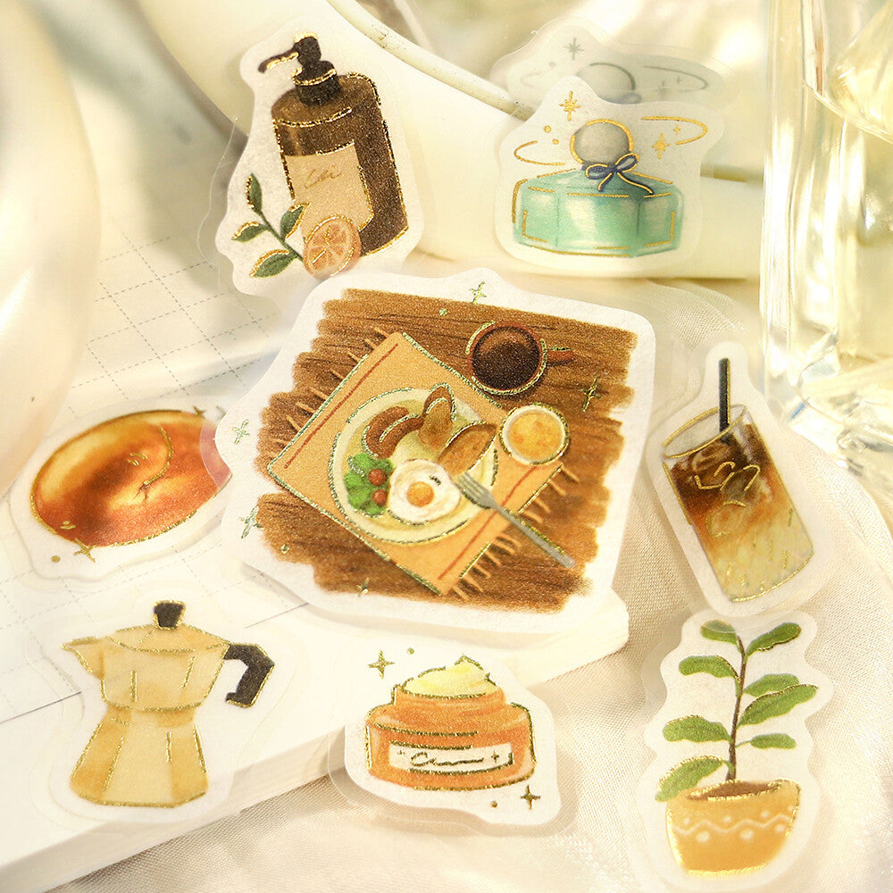 A close-up of a sliced bread or pastry topped with cute illustrated stickers, surrounded by more matching sticker designs on a cloth surface.

