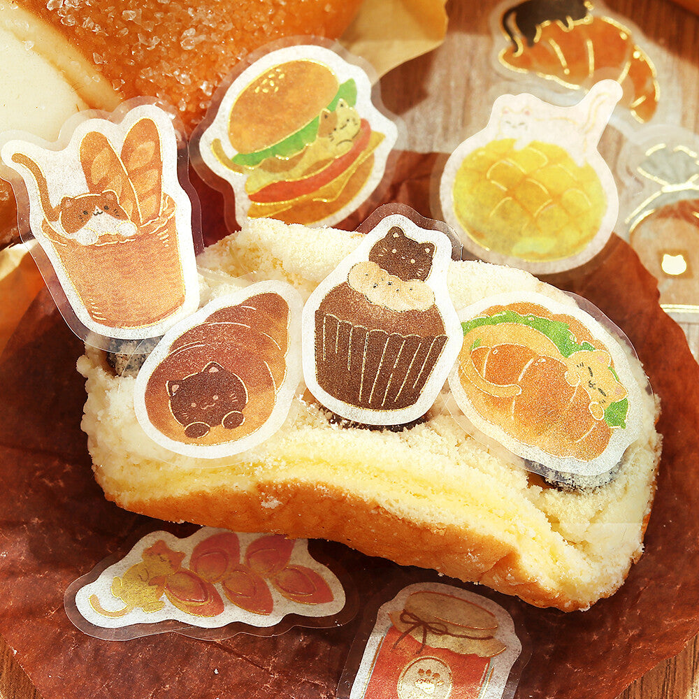 A close-up of a sliced bread or pastry topped with cute illustrated stickers, surrounded by more matching sticker designs on a wooden surface.