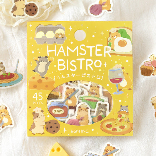 A package of 45 cute hamster-themed stickers displayed on a white textured fabric background. The packaging is bright yellow with illustrations of hamsters in a bistro setting, and the clear window reveals the assorted stickers inside.