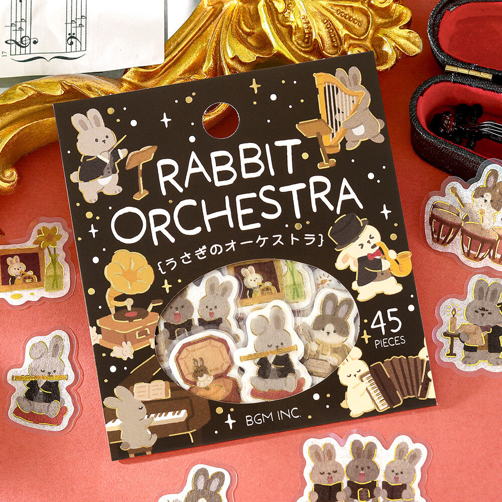 Rabbit Orchestra sticker pack by BGM INC, featuring 45 cute bunny orchestra stickers on a decorative black backing card, surrounded by loose stickers on a red surface with gold and black decorative props.