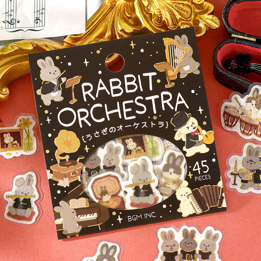 Rabbit Orchestra sticker pack by BGM INC, featuring 45 cute bunny orchestra stickers on a decorative black backing card, surrounded by loose stickers on a red surface with gold and black decorative props.
