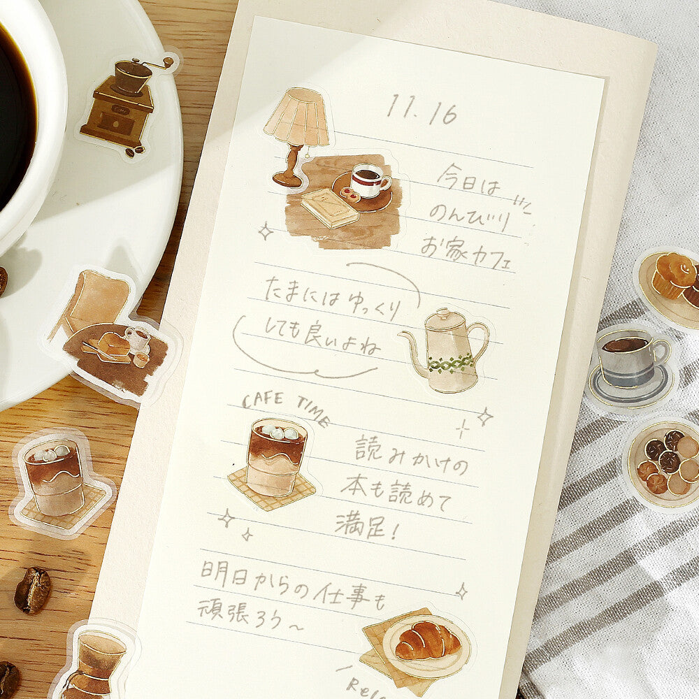 Notebook with illustrated coffee-themed stickers on a wooden surface with a cup of coffee.