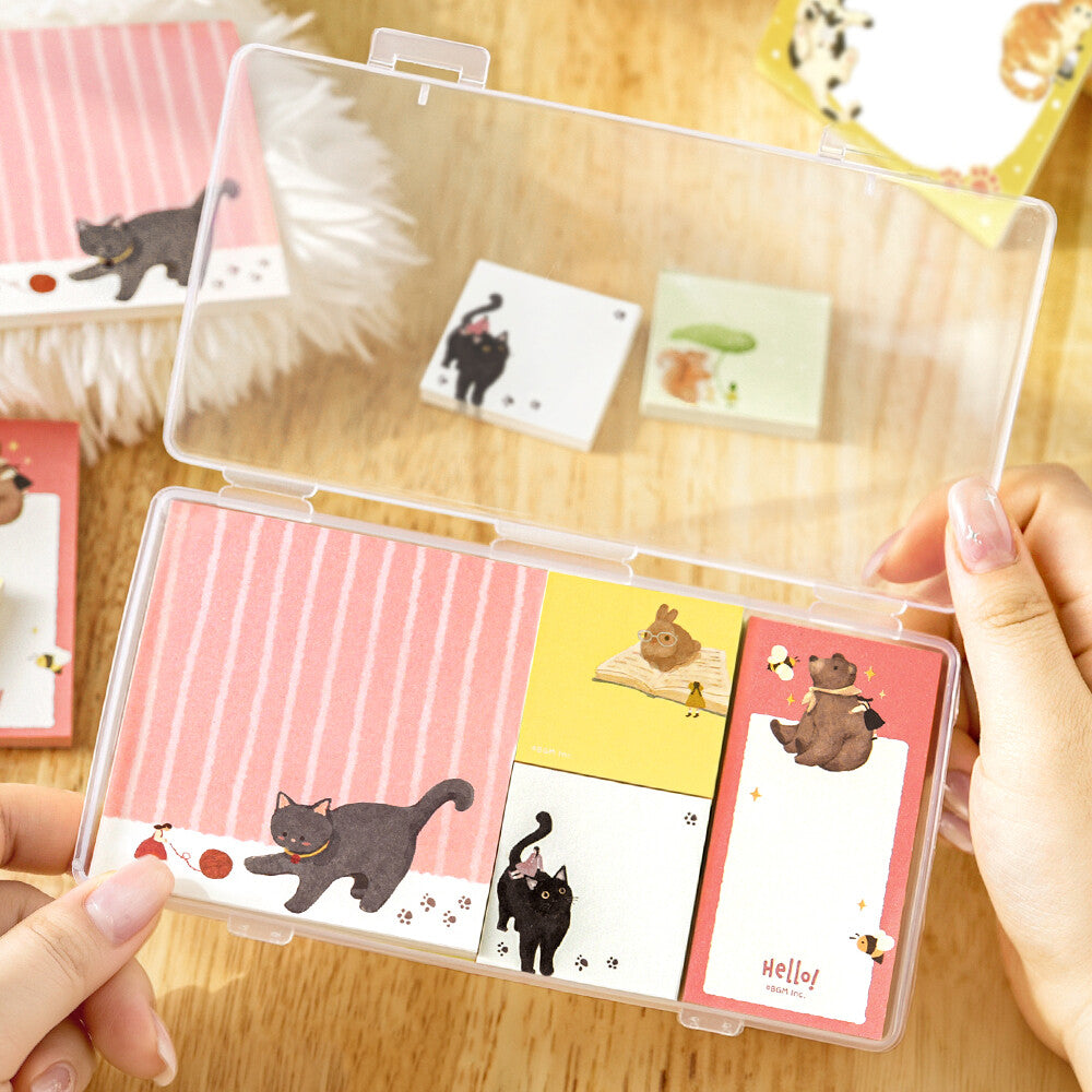 Two hands opening a clear package of memo pads. The memo pads are decorated with a animal illustrations on a wood surface background