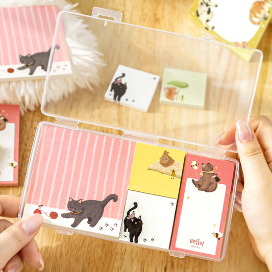 Two hands opening a clear package of memo pads. The memo pads are decorated with a animal illustrations on a wood surface background