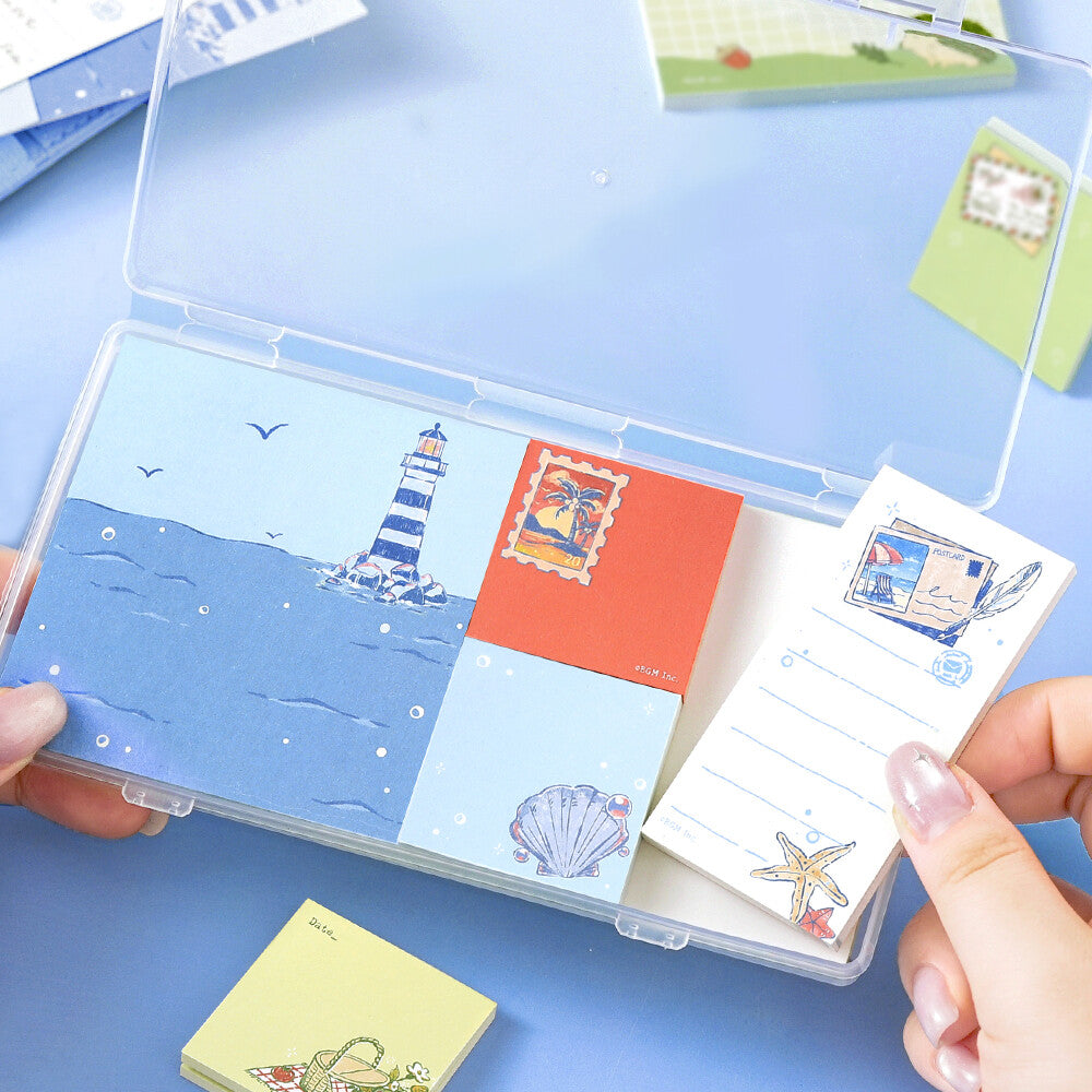 Two hands opening a clear package of memo pads. The memo pads are decorated with a travel theme on a blue background

