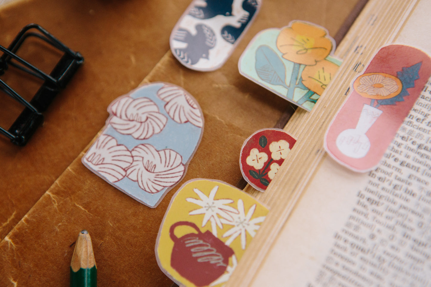 Decorative paper clips with floral designs on a wooden surface.