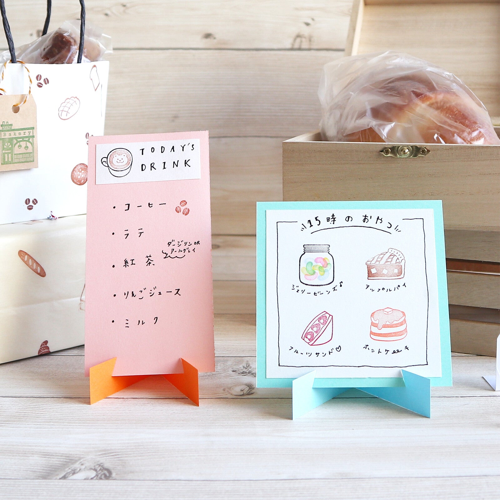 Two small signs on stands, one pink with text and the other blue with illustrations, against a wooden background.