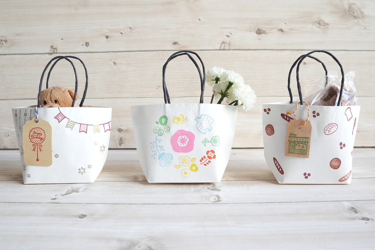Three decorative paper bags with handles on a wooden surface