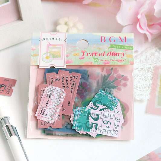 A package of BGM Travel Diary deco stickers displayed on a white surface with a pink floral background. The stickers include pink ticket designs, green train schedule sheets, and floral elements, with the packaging header reading 'BGM Travel diary'.