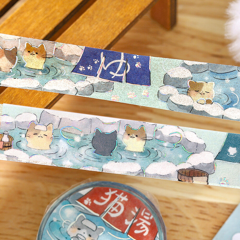 Decorative washi tape with cartoon cats in a hot spring design on a wooden surface.