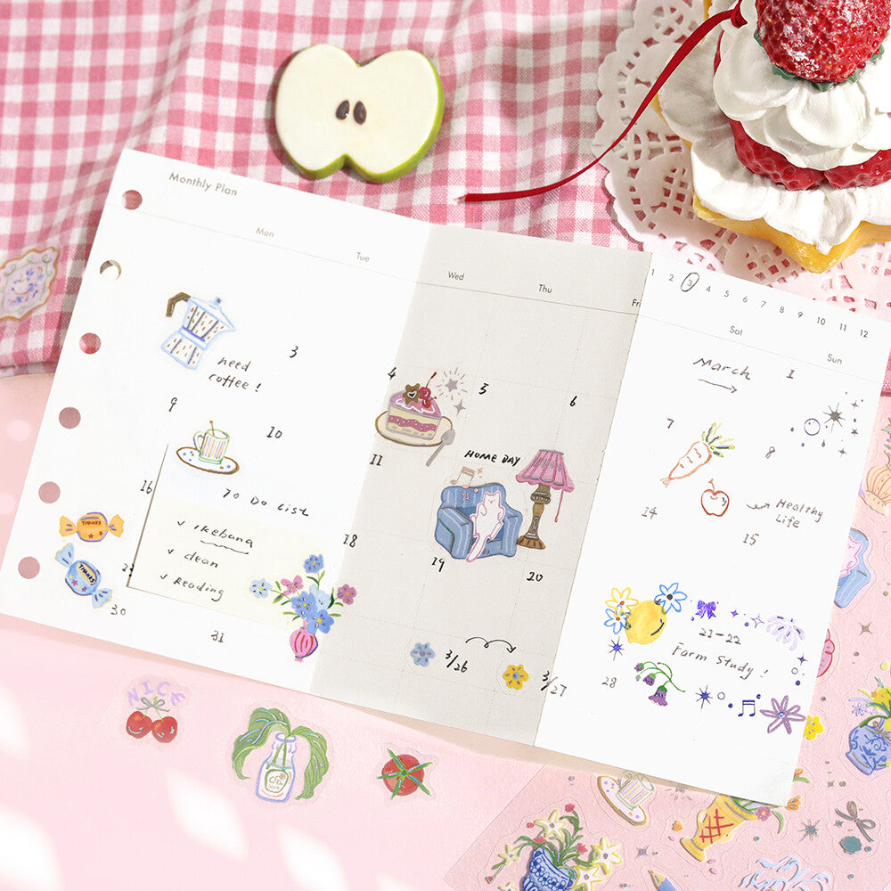 Two illustrated planners on a pink checkered tablecloth with a cake and apple slice.