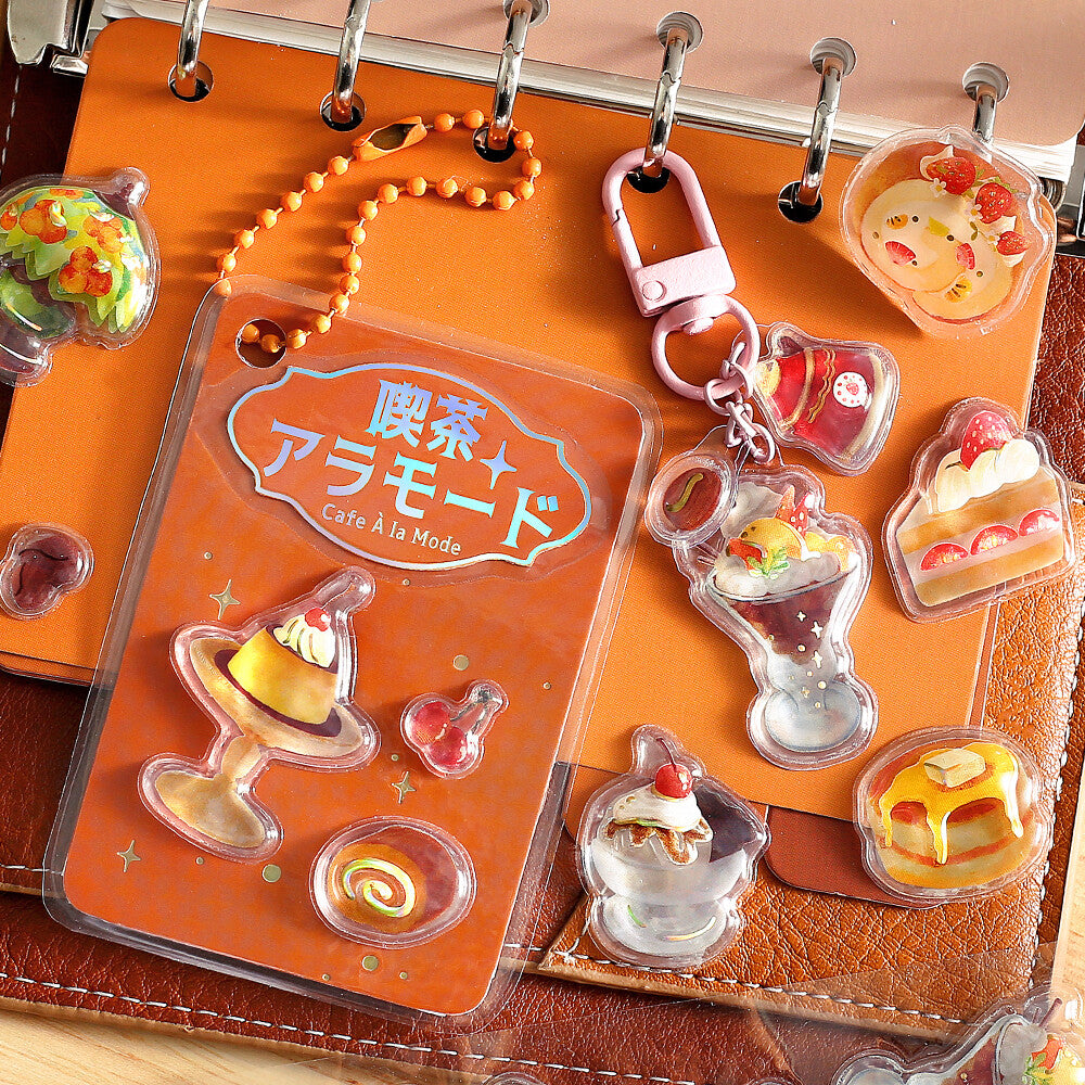 Set of dessert-themed keychains on an orange card with Japanese text, displayed on a leather surface.