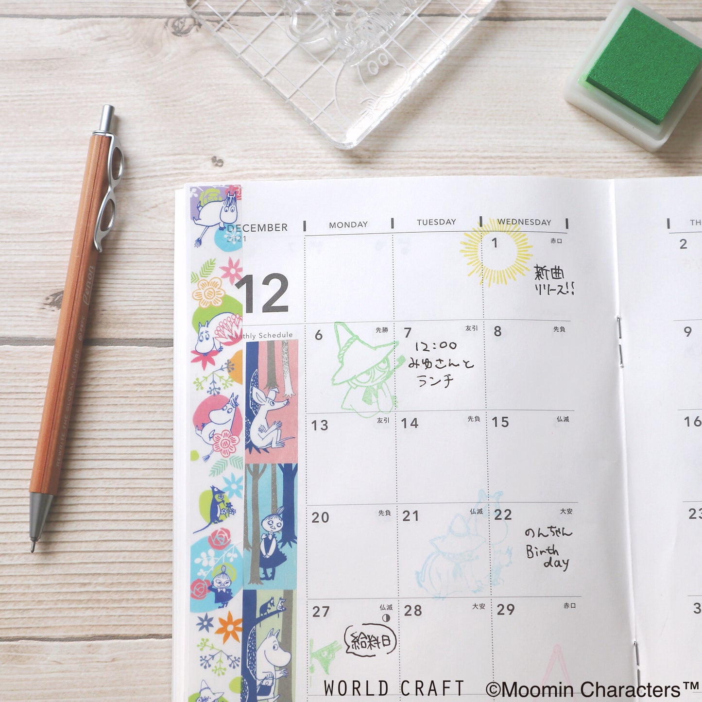 Calendar with Moomin characters on a wooden surface with stationery items.
