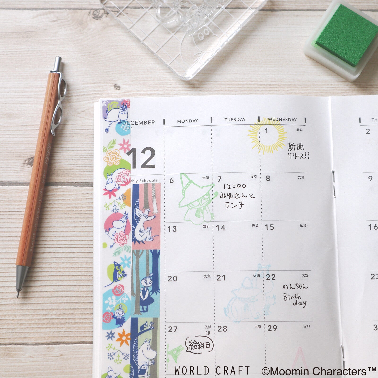 Calendar with Moomin characters on a wooden surface with stationery items.